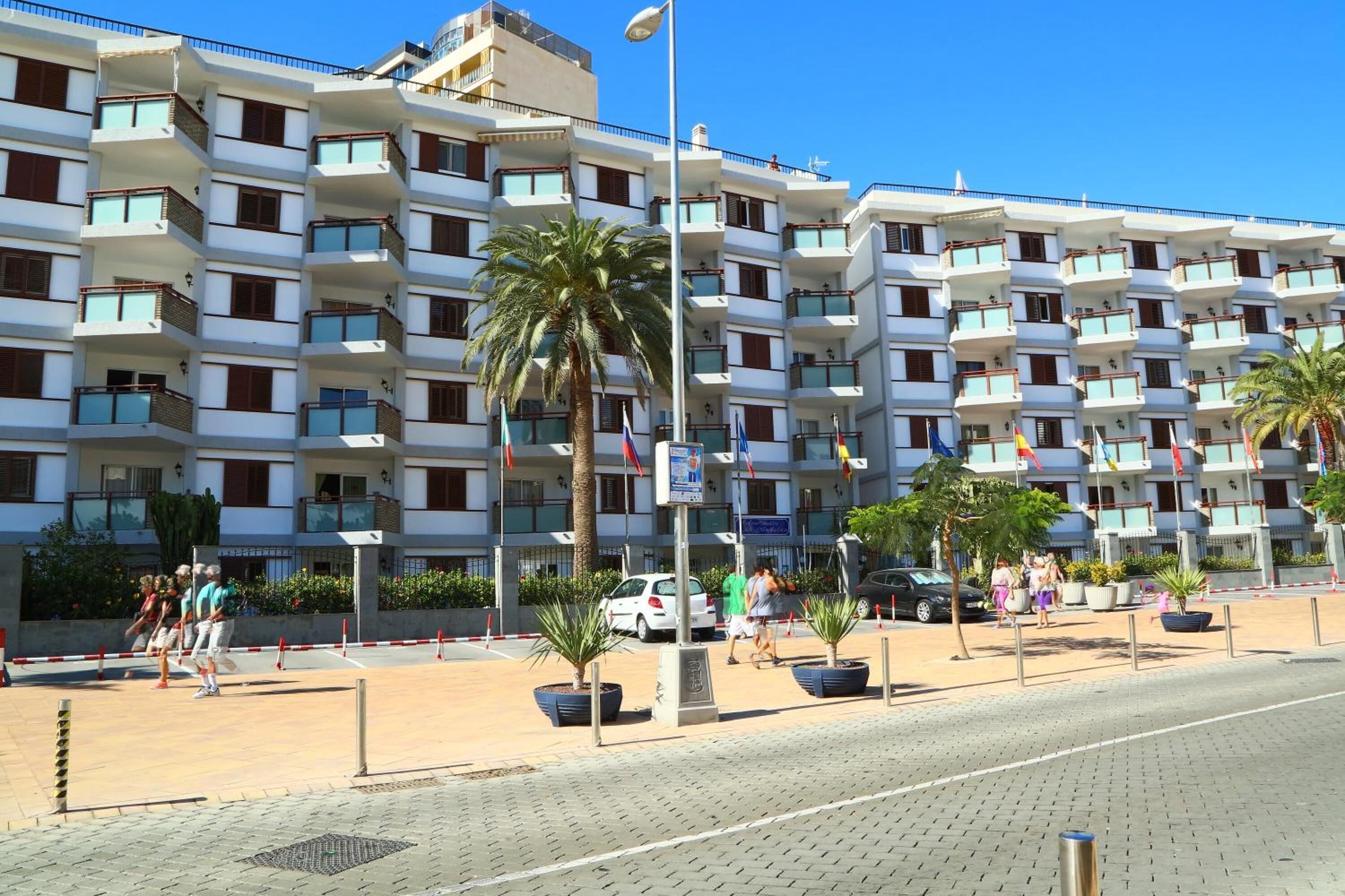 Ein mehrgeschossiges Hotel mit Balkonen, Palmen und einem gepflasterten Weg.