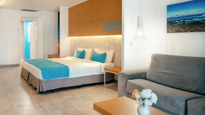 A modern hotel room with a bed, a sofa, a small table, and a painting on the wall.