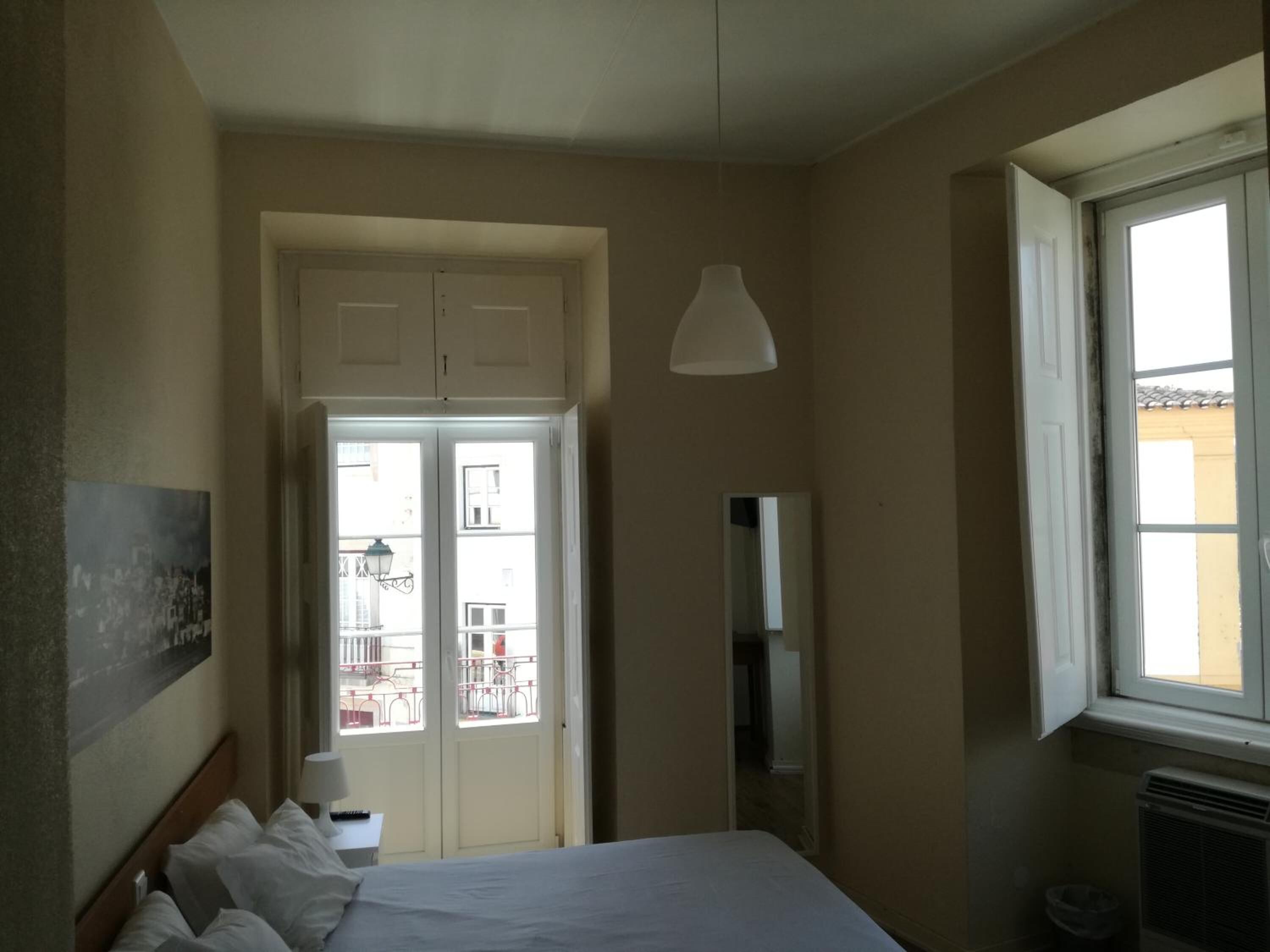 Ett hotellrum med en säng, ett fönster, en dörr och en spegel.