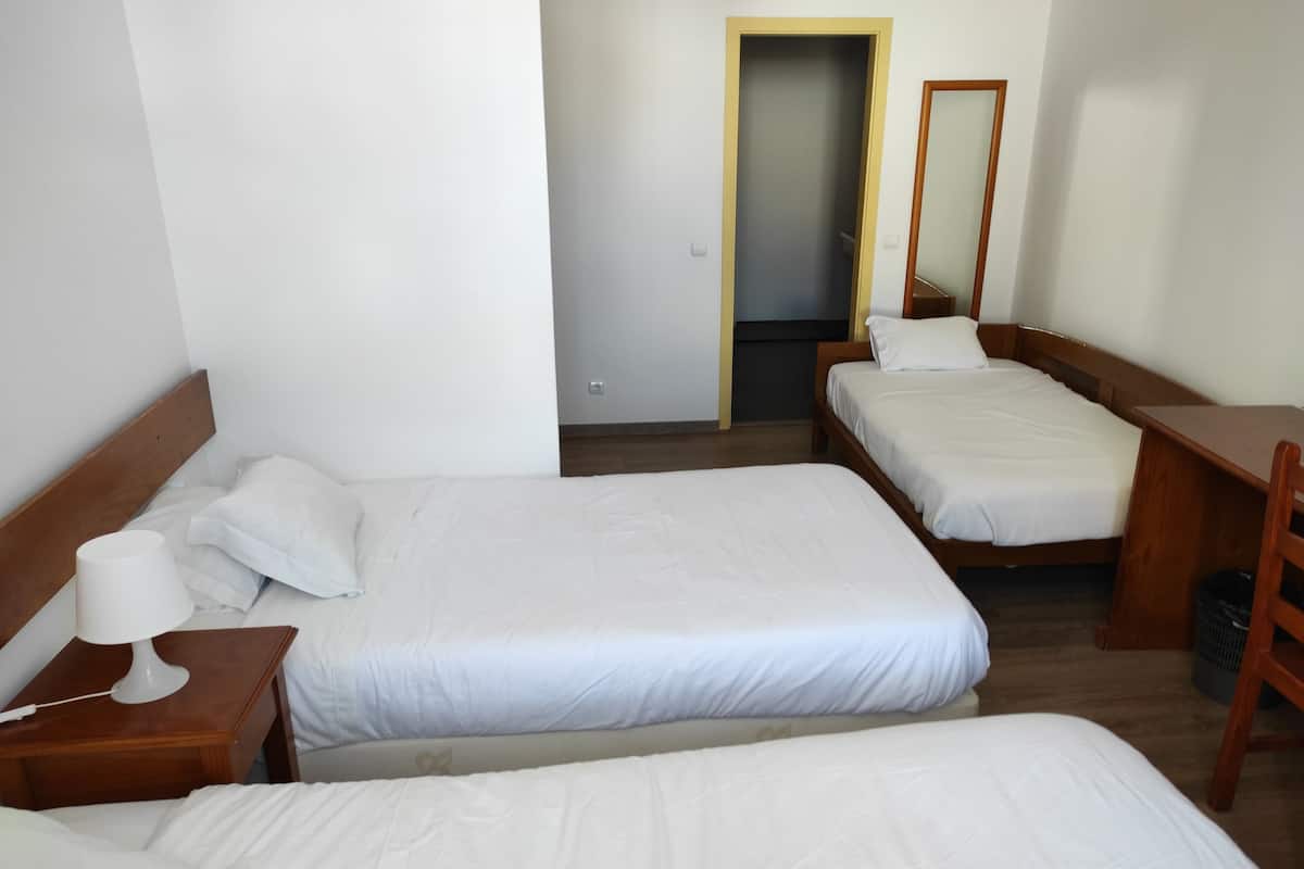 A hotel room with two single beds, a wooden nightstand with a lamp, a small table, and a mirror.