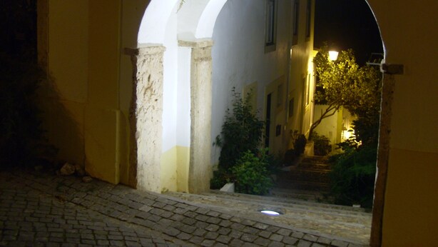 Un arco de entrada que da a una calle tenuemente iluminada de noche.