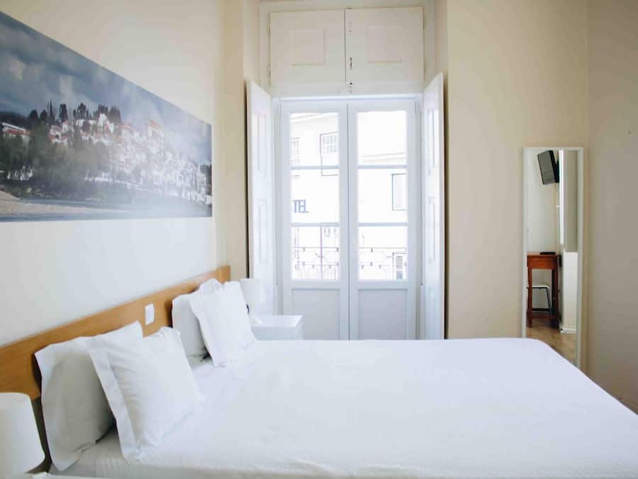A hotel room with a large bed, a painting on the wall, and a view through the door.