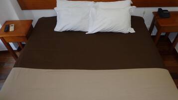 A bed with a brown bedspread and two white pillows, flanked by wooden nightstands with a remote control and a phone on one.
