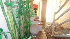 Una escalera con piso de baldosas que conduce a un nivel superior, rodeada de follaje y un muro de piedra.