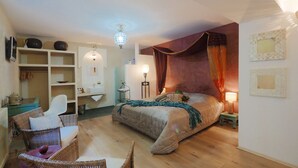 Une chambre à coucher avec un grand lit, une table de chevet avec une lampe, une armoire, une chaise et une petite table sur laquelle est posé un objet décoratif.