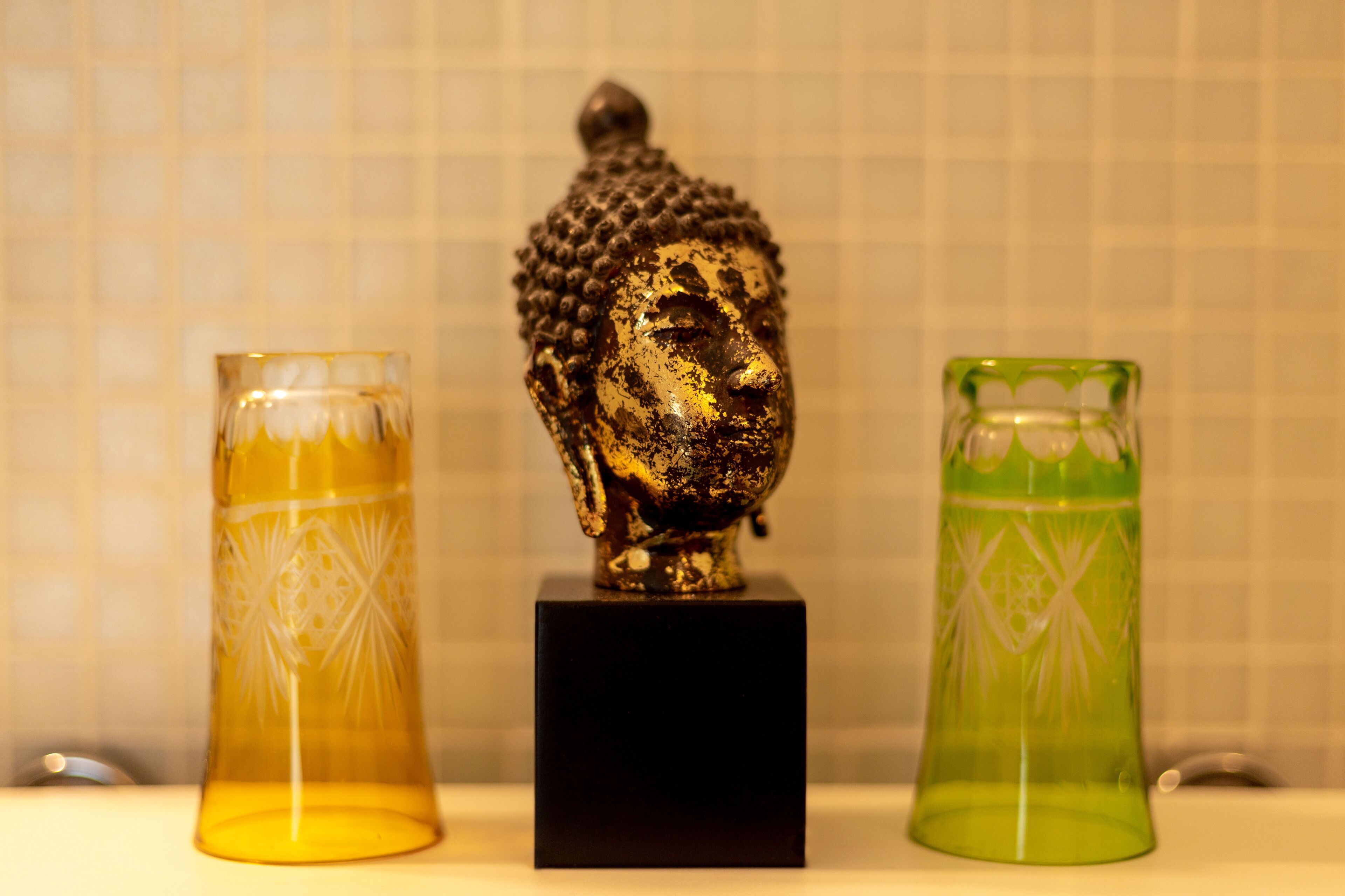 Uma estátua de Buda sobre um pedestal preto, entre dois recipientes de vidro com padrões geométricos.