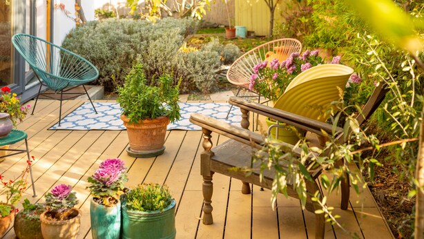 Une terrasse en bois agrémentée de plantes en pot, un tapis à motifs bleus et deux fauteuils en osier.