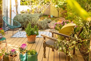 A wooden deck with potted plants, a blue patterned rug, and two wicker chairs. - The Rooms Bed & Breakfast (Vienna)