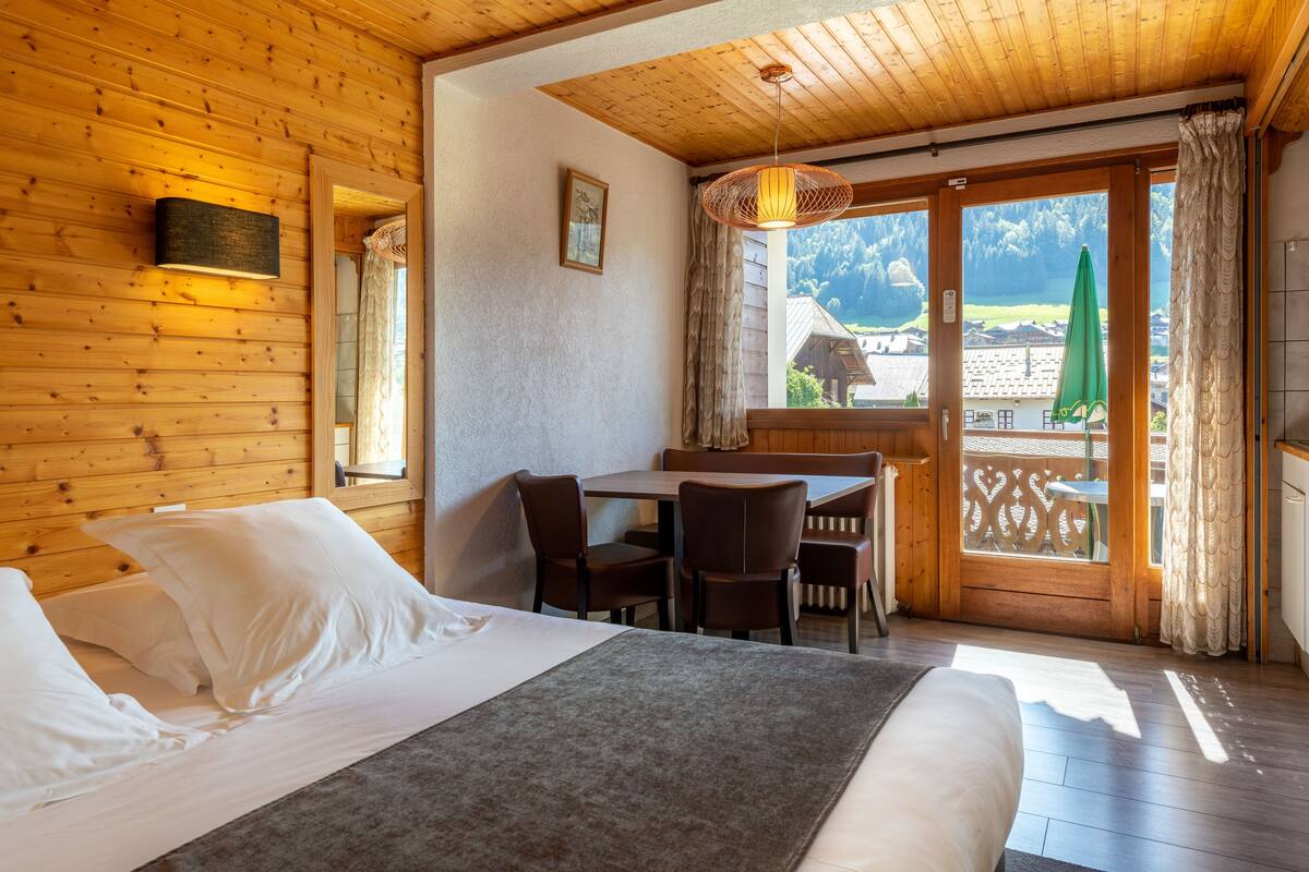 Una habitación de madera con una cama, una mesa y sillas, y vistas al exterior.