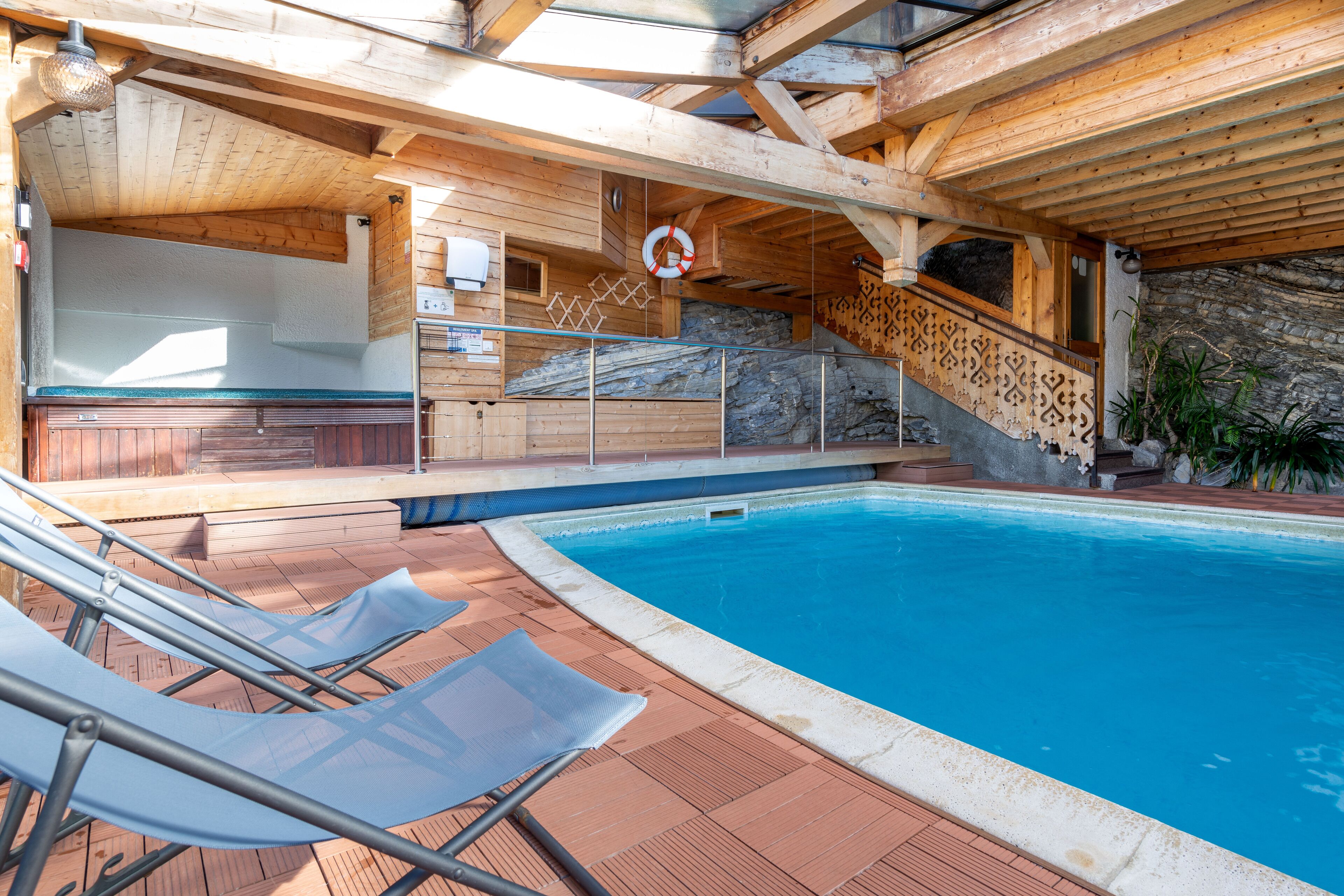 A wooden pool area with lounge chairs, a stone wall, and a staircase.