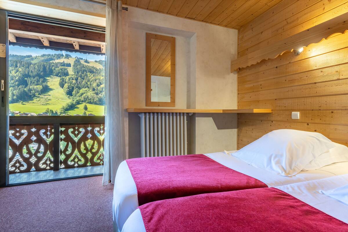 Un dormitorio con dos camas, techo de madera, ventana con vistas a un paisaje verde y un espejo en la pared.
