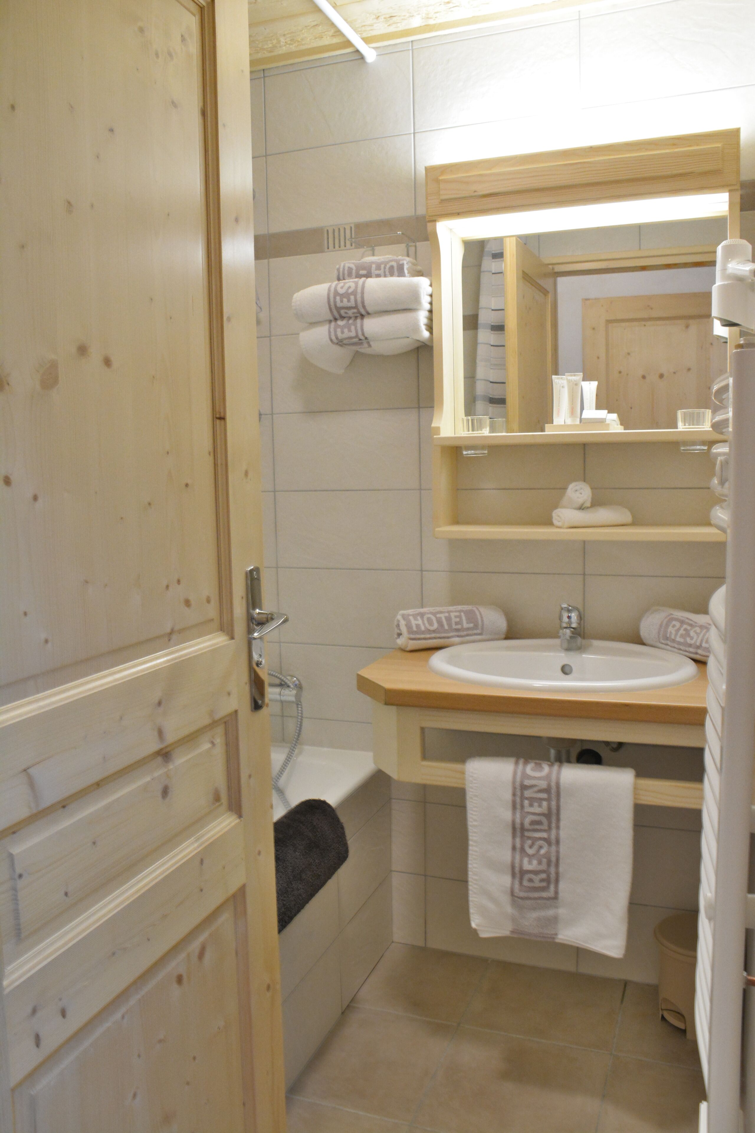 Une salle de bain avec une porte en bois, un lavabo, un miroir, un porte-serviettes et une douche.