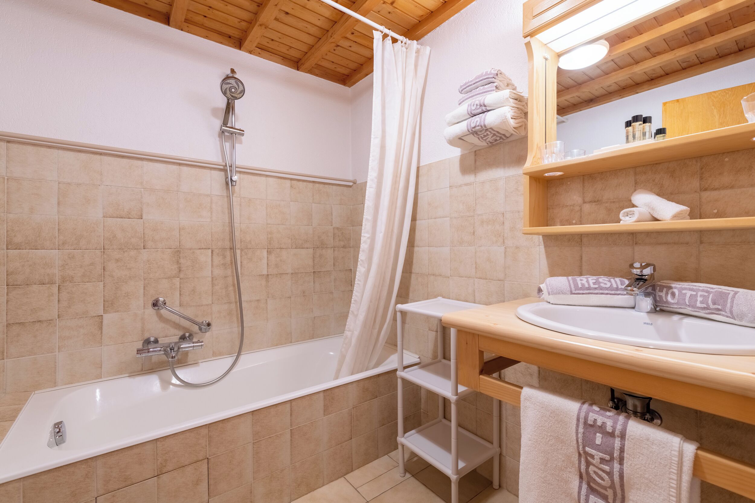 A bathroom with a bathtub, shower, wooden shelves with towels, and a mirror.
