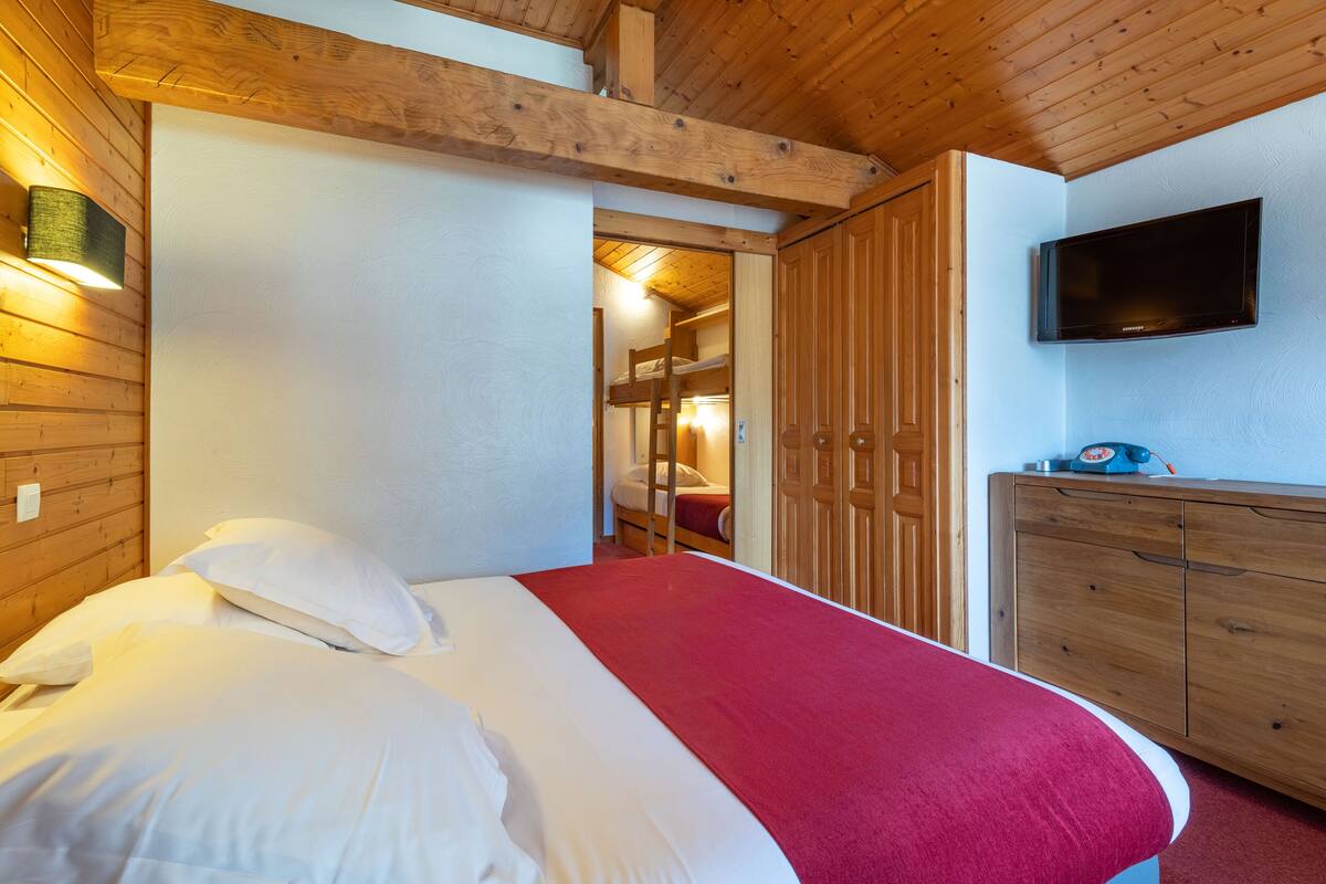 Un dormitorio con cama, armario de madera y televisor en la pared.
