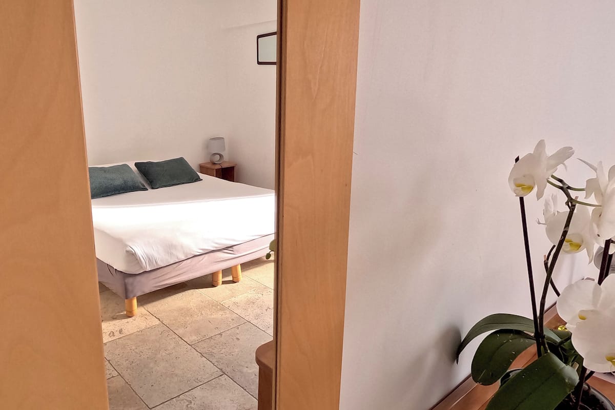 Un dormitorio con cama, almohadas, una mesita de noche y una orquídea en maceta.