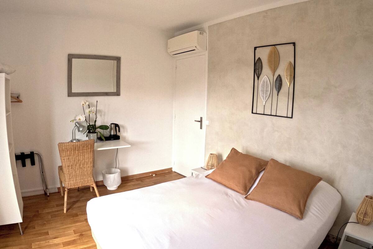 Un dormitorio con una cama grande, un escritorio con una silla, un aire acondicionado instalado en la pared y una obra de arte enmarco.