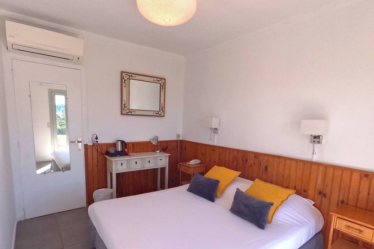 Habitación de hotel con una cama grande, mesitas de noche, un escritorio con lámpara, un espejo y una luz en el techo.