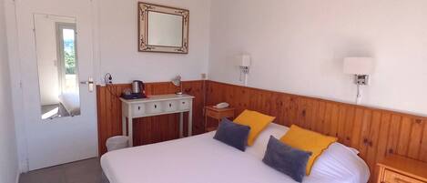 A hotel room with a large bed, bedside tables, a desk with a lamp, a mirror, and a ceiling light.