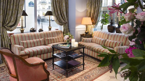 A living room with striped sofas, a coffee table, and a chair. There are curtains, a lamp, and a vase with flowers. - Le Relais Saint Honoré (Paris)