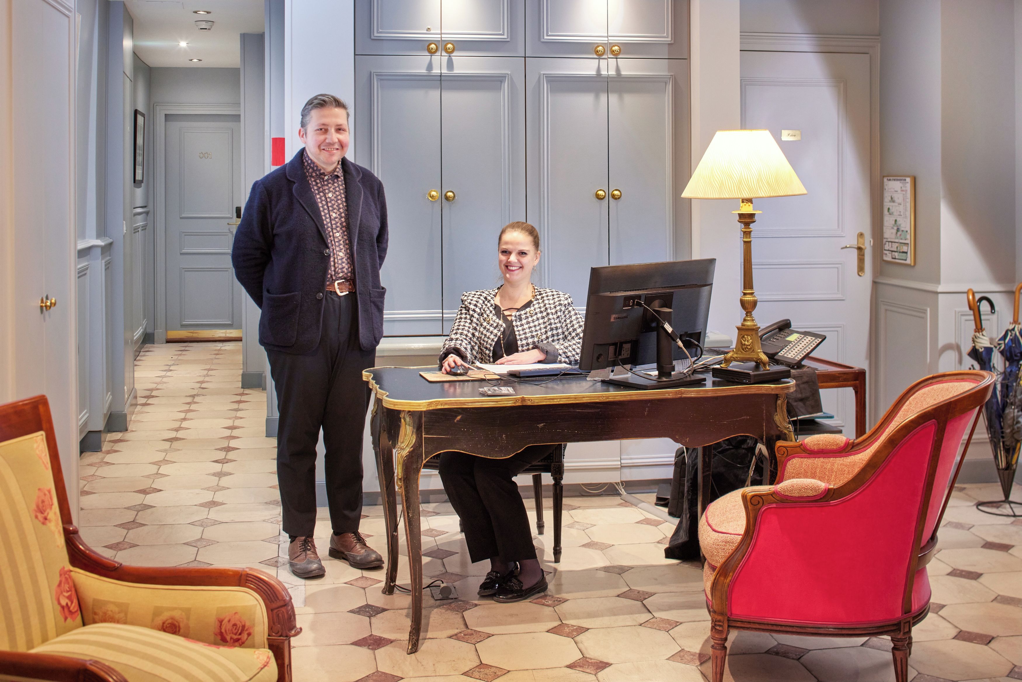 Un hall d’hôtel avec un comptoir d’accueil, un ordinateur, une lampe et un téléphone.