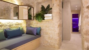 A stone-walled room with a wooden bench, a mirror, and a plant. - Le Relais Saint Honoré (Paris)