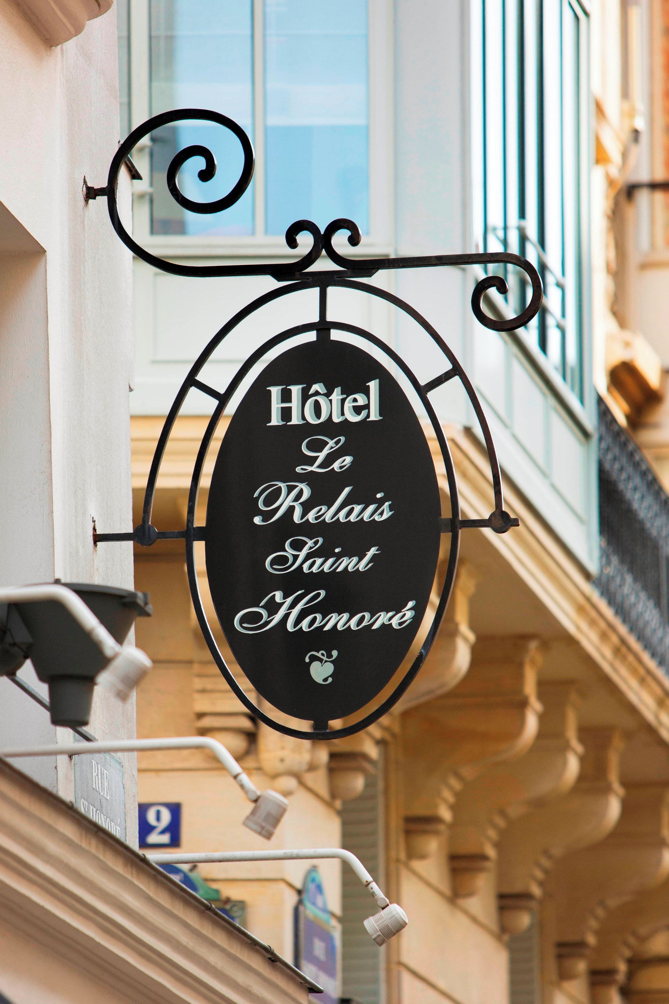 A hotel sign with the name 'Hôtel Le Relais Saint Honoré' in a classic font, mounted on a metal bracket with decorative scrollwork.