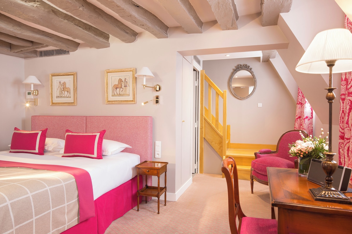 A hotel room with a bed, a desk, a chair, a mirror, and a staircase.