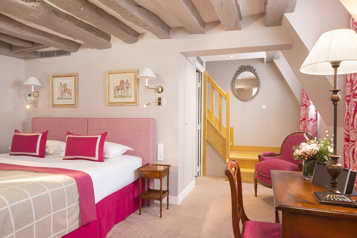 A hotel room with a bed, a desk, a chair, a mirror, and a staircase.
