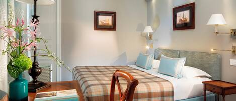 Ein Hotelzimmer mit einem Bett, zwei Nachttischen, einem Sessel, einer Lampe und zwei gerahmten Bildern an der Wand.