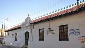 Un edificio blanco con techo de tejas rojas, una pequeña estructura abovedada y un letrero que dice “Hotel”. 