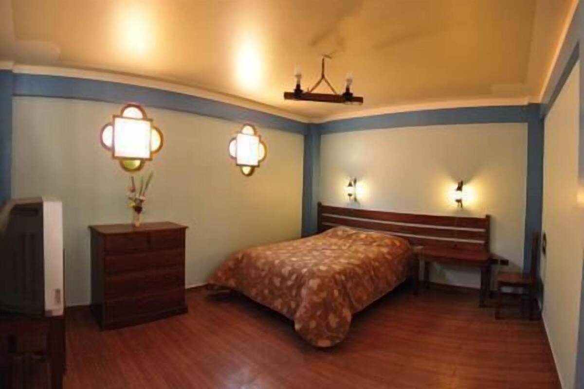 Un dormitorio con una cama de madera, un aparador y dos lámparas fijadas a la pared.