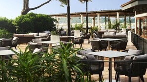 Une terrasse extérieure aménagée avec des meubles en osier, des tables et des plantes en pot.