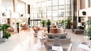 Un hall d’entrée spacieux avec un espace salon central, de grandes fenêtres et des plantes d’intérieur.