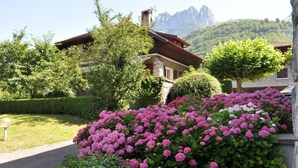 A house with a stone facade, surrounded by lush greenery and pink flowers. - Hotel Du Lac (Talloires-Montmin)