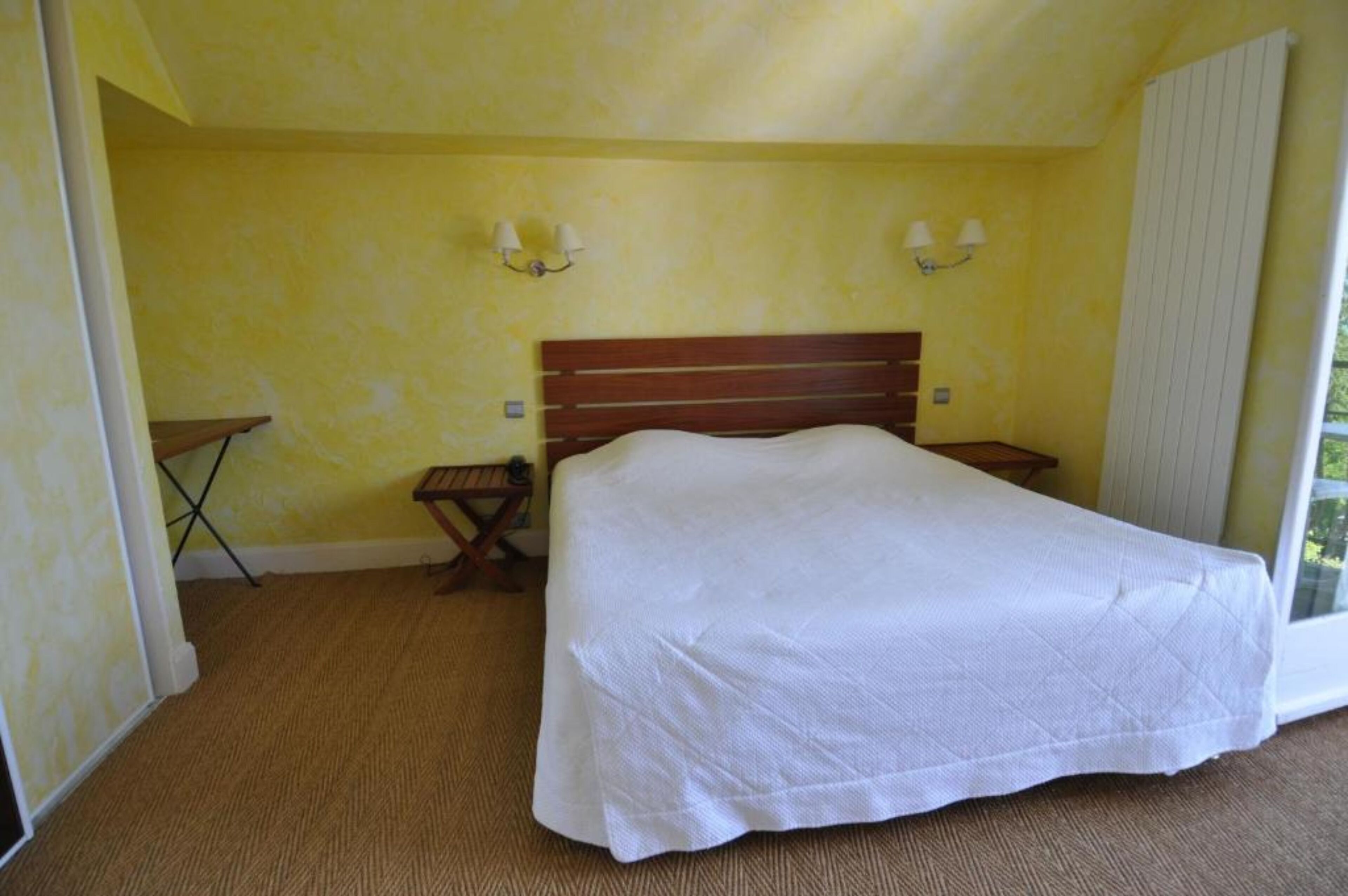 Un dormitorio con una cama grande, dos mesitas de noche, una mesita pequeña y un radiador.