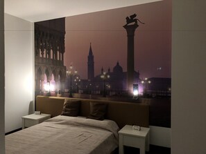 A hotel room with a large bed, two bedside tables, and a wall mural of a cityscape at dusk. - Hotel Angi (Fosso)