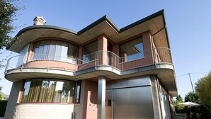 A modern two-story house with a curved balcony, a garage, and a well-maintained garden. - Hotel Angi (Fosso)