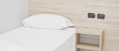 Un dormitorio minimalista con cabecera de madera, una cama blanca y una mesita de noche de madera con dos interruptores.