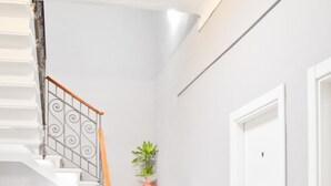 A staircase with white walls and a wooden handrail, leading to a door with a potted plant beside it. - Miu Hotel (Milan)
