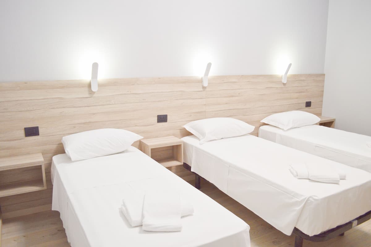 Una habitación de hotel con tres camas individuales, cada una con colchón y almohada blancos, y cabeceros de madera.