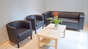 Ein modernes Wohnzimmer mit einer dunkelbraunen Ledersofa, zwei Sesseln und einem Holztisch mit einer Pflanze.