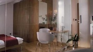 A modern hotel room with a bed, a white chair, a small table, and a plant. - Musketyr (Prague)
