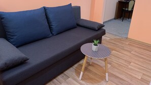 A dark gray sofa with two cushions, a small round table with a geometric pattern, and a potted plant. - Pension City Center (Prague)