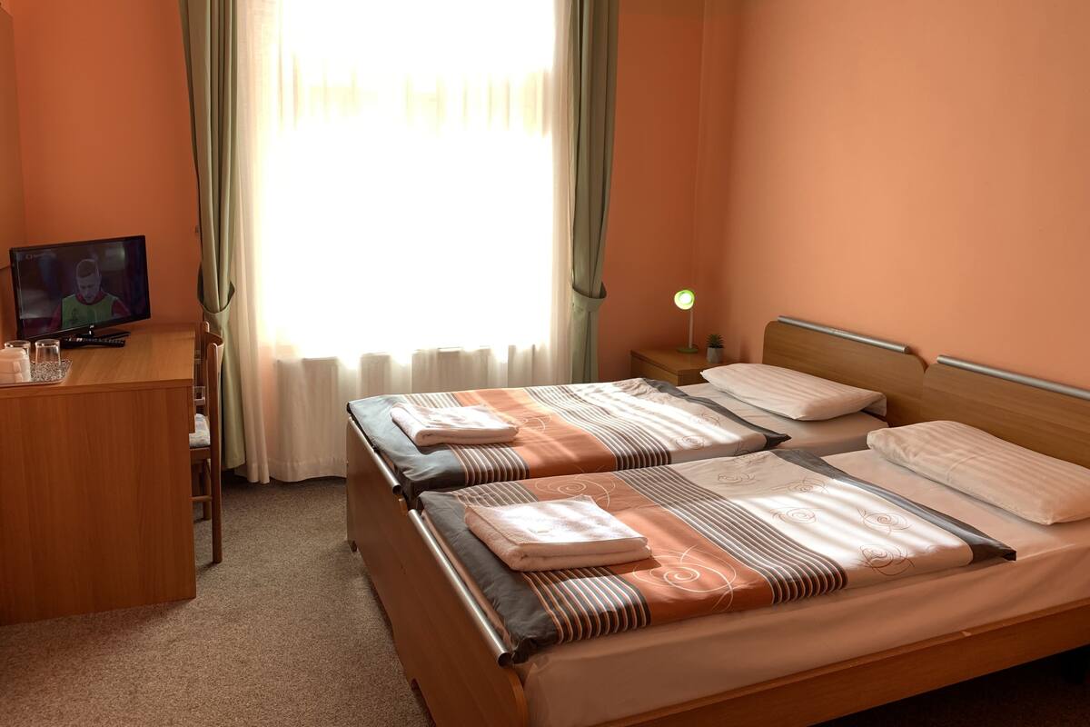 Habitación de hotel con dos camas, un escritorio con televisor, una lámpara de noche y una ventana con cortinas.