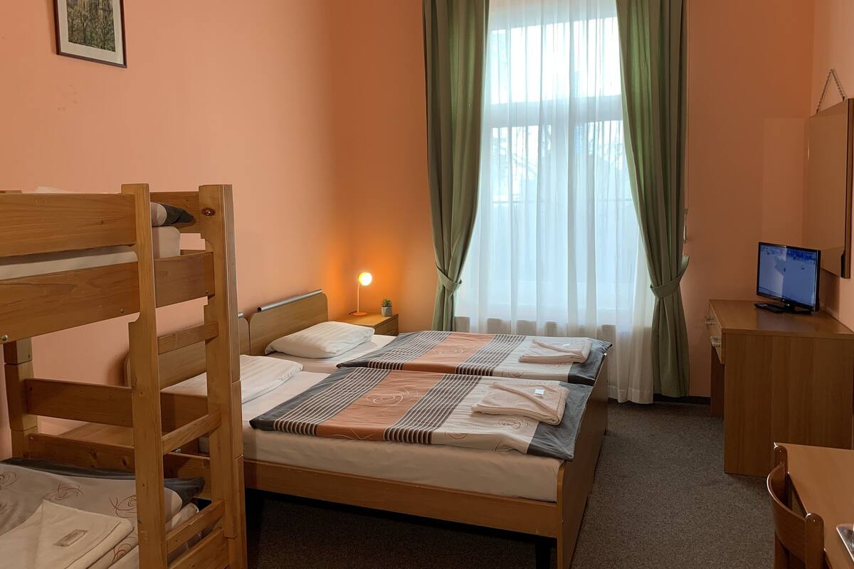 Un dormitorio con una cama litera, un escritorio con computadora, una lámpara de noche y una ventana con cortinas.