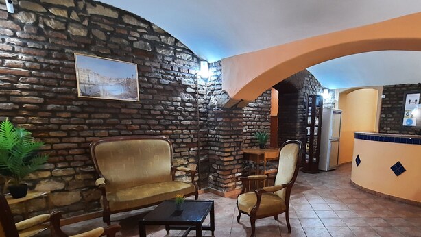 A cozy room with a stone wall, a wooden sofa, a wooden chair, a small table, and a counter with a plant. - Pension City Center (Prague)