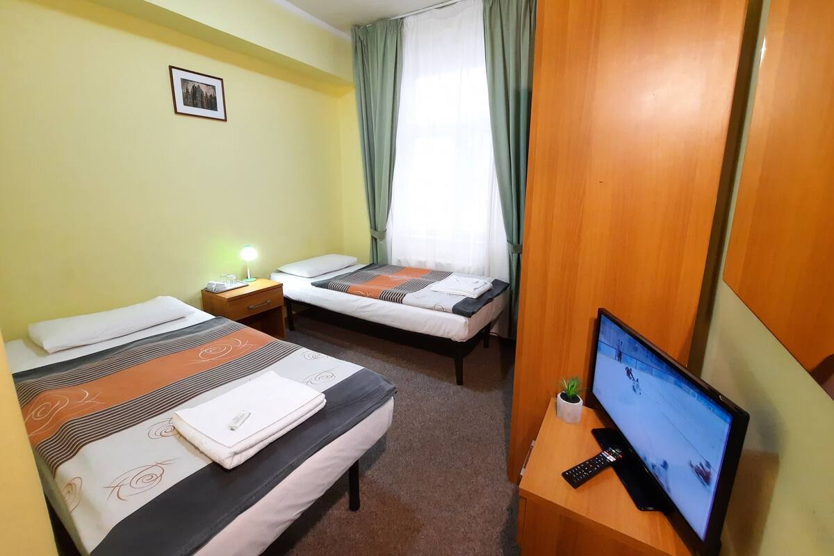 Una habitación de hotel con dos camas, un escritorio con televisor, una mesita de noche y una ventana con cortinas.