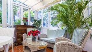 Una habitación iluminada por el sol con muebles de mimbre, una mesa de centro de cristal y una gran planta en maceta.