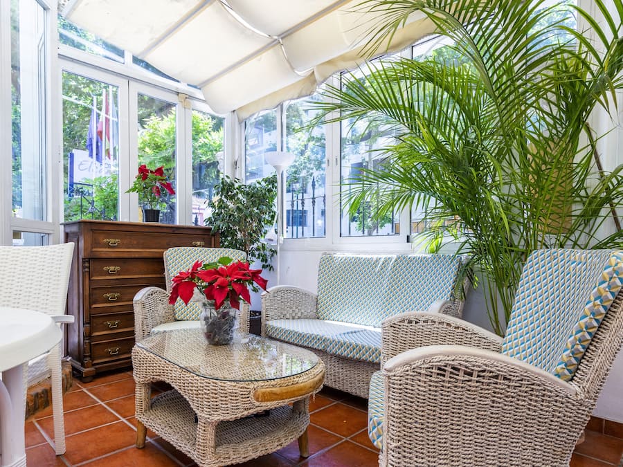 Una habitación iluminada por el sol con muebles de mimbre, una mesa de centro de cristal y una gran planta en maceta.