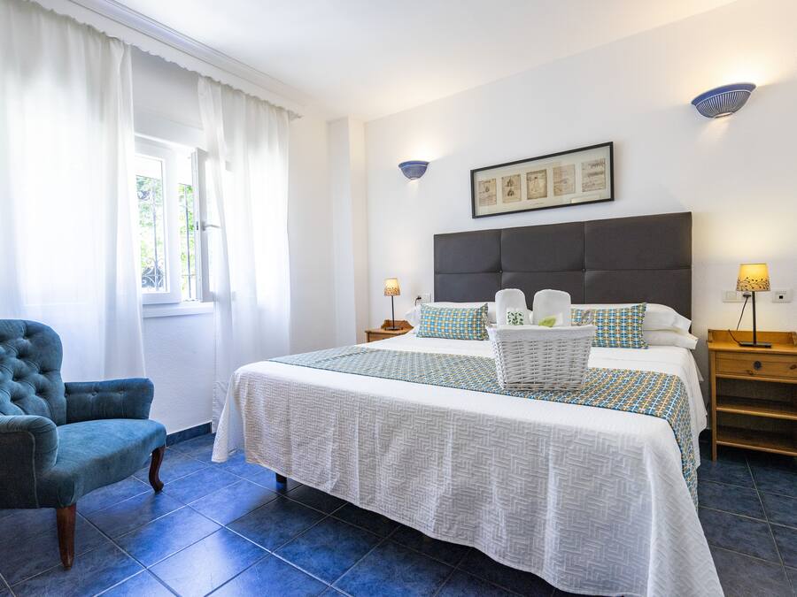 Une chambre à coucher avec un grand lit, une chaise, une table de chevet et une lampe fixée au mur.